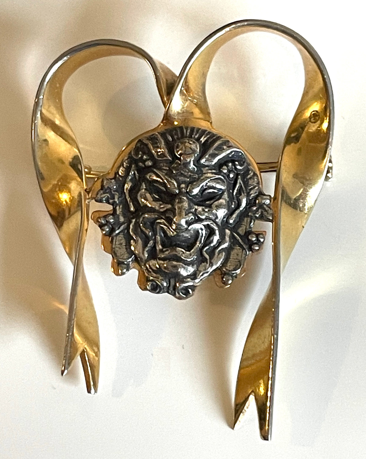 Unusual vintage 'Bacchus' face brooch with silver tone mounted on gold tone ribbon motif, French machine age construction, trombone clasp