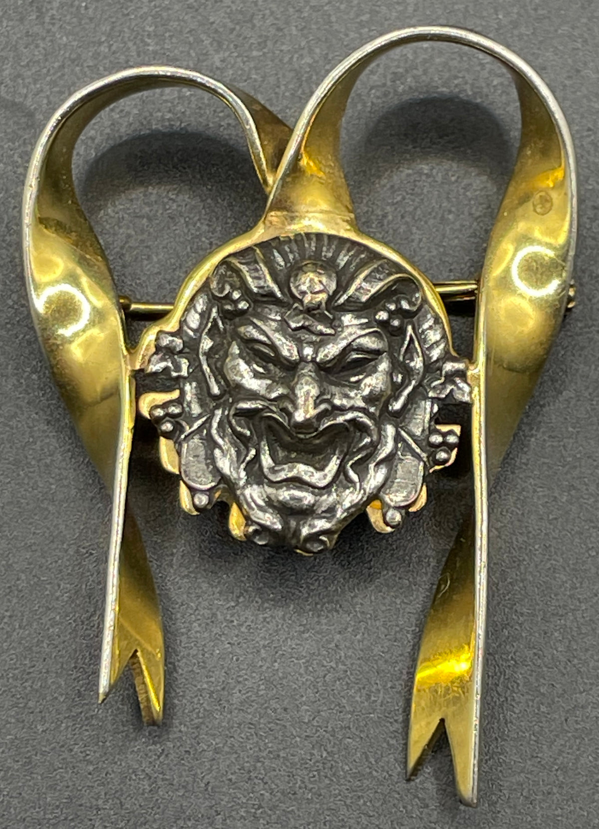 Unusual vintage 'Bacchus' face brooch with silver tone mounted on gold tone ribbon motif, French machine age construction, trombone clasp