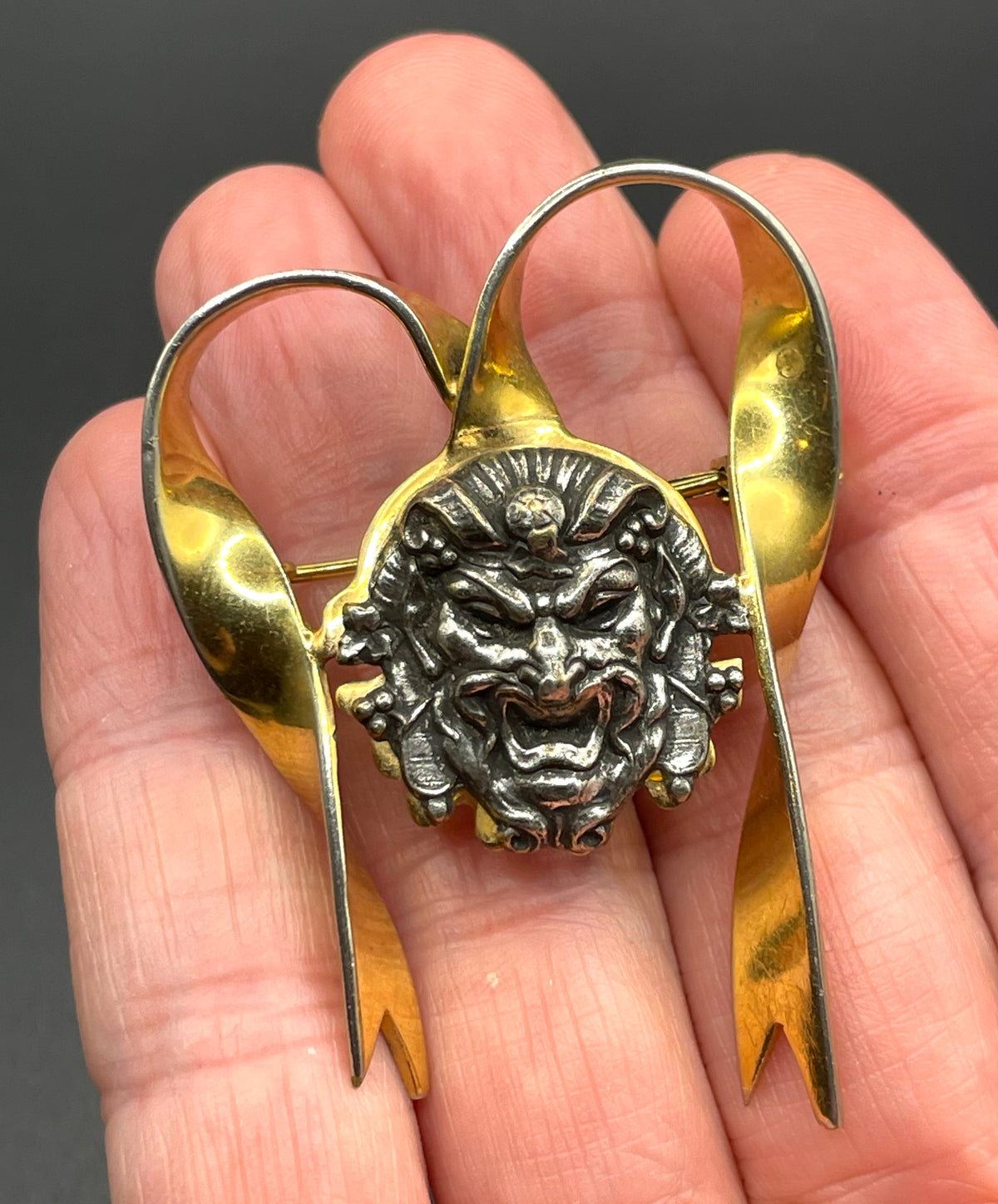 Unusual vintage 'Bacchus' face brooch with silver tone mounted on gold tone ribbon motif, French machine age construction, trombone clasp