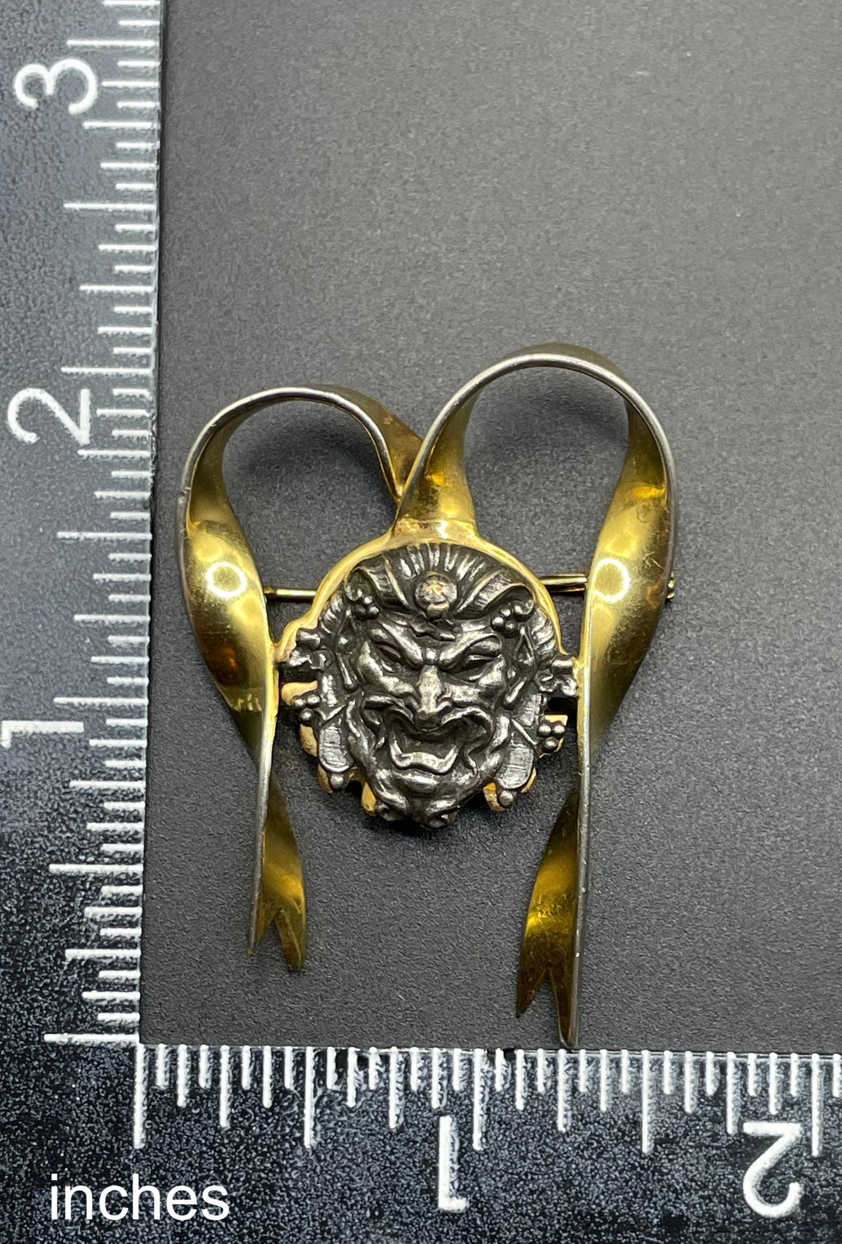 Unusual vintage 'Bacchus' face brooch with silver tone mounted on gold tone ribbon motif, French machine age construction, trombone clasp