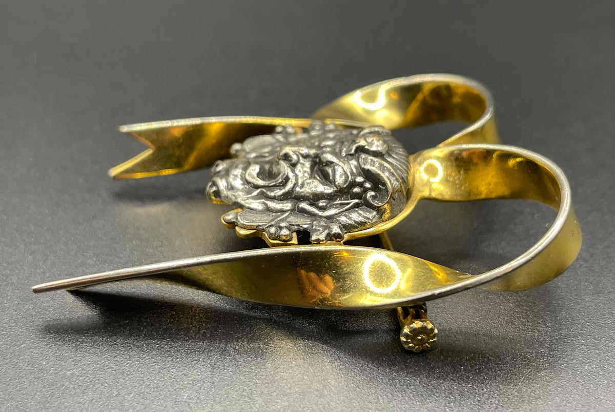 Unusual vintage 'Bacchus' face brooch with silver tone mounted on gold tone ribbon motif, French machine age construction, trombone clasp