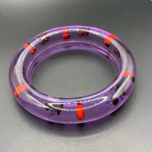 Vintage inclusion bangle with ants and red accents in transparent purple lucite style plastic resin, gives a glow under ultraviolet UV light